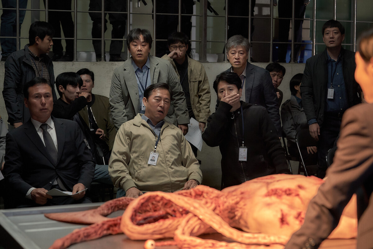 Kim In-kwon as Kang Won-seock and Kwon Hae-hyo as Kim Chul-min stare at a creature on a steel table in a still image from the series ‘Parasyte: The Grey.’