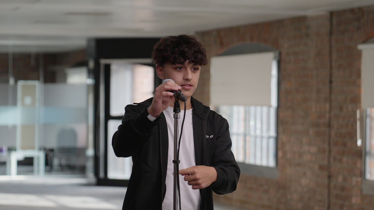 Young man adjusting a microphone in a modern office with exposed brick walls and large windows, natural daylight creating a calm, focused atmosphere.