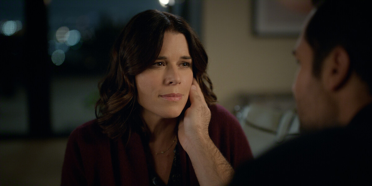 A woman looks thoughtfully at a man who gently holds her face, sitting together in a softly lit, cozy indoor setting at night, conveying a sense of intimacy and emotional connection.