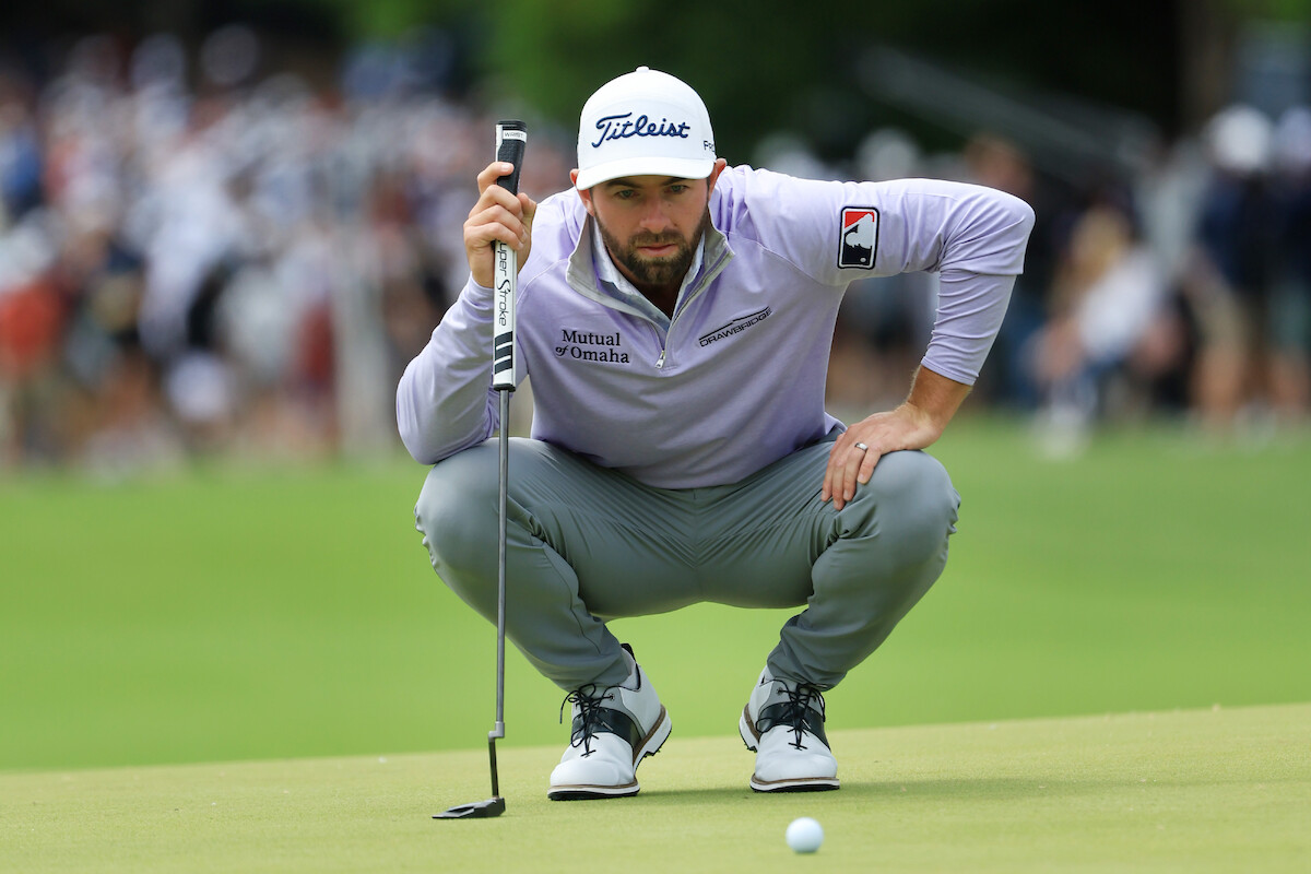 Golfer Cameron Young crouches down to scrutinize a putt.