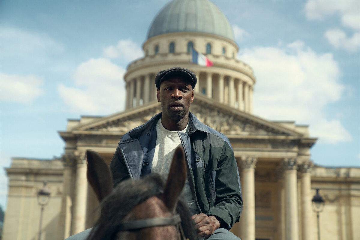 Homem negro de casaco e chapéu aparece montado em um cavalo em frente a um prédio oficial francês