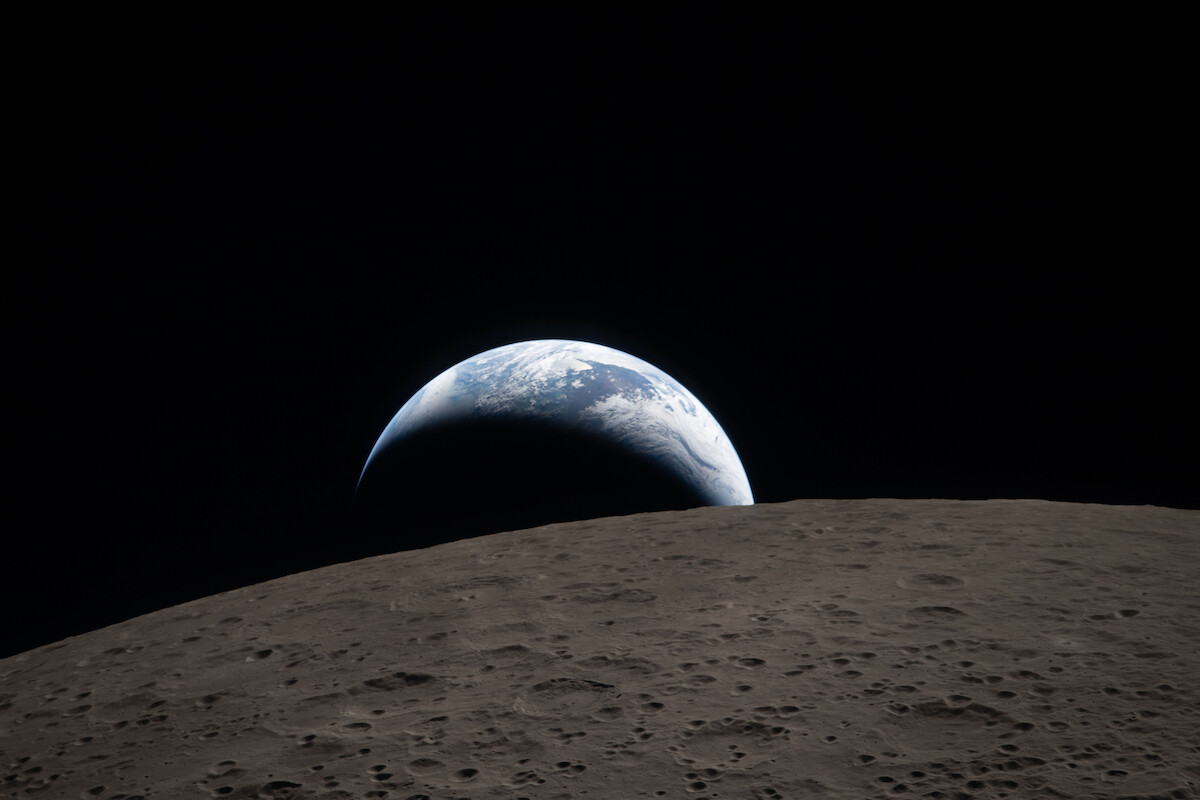 Earth rising over the moon’s horizon, captured from space with the moon’s cratered surface in the foreground and the dark expanse of space in the background.