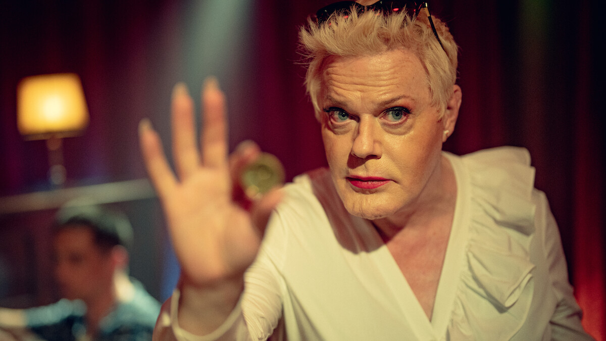 Eddie Izzard as Lachy holds up a gold coin in Season 1 of ‘Kaos’