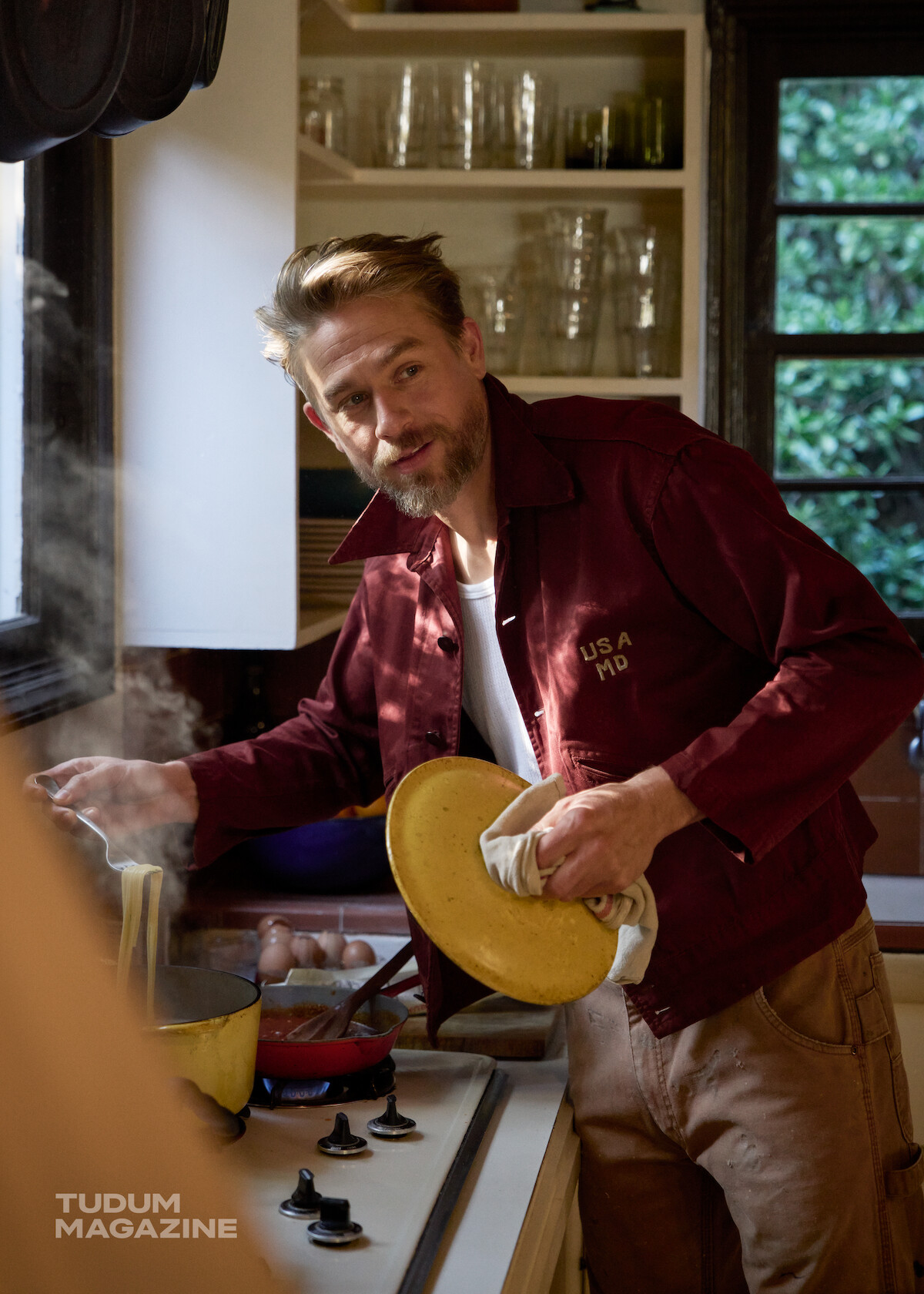 Charlie Hunnam cooks pasta in a kitchen on a gas stove top.