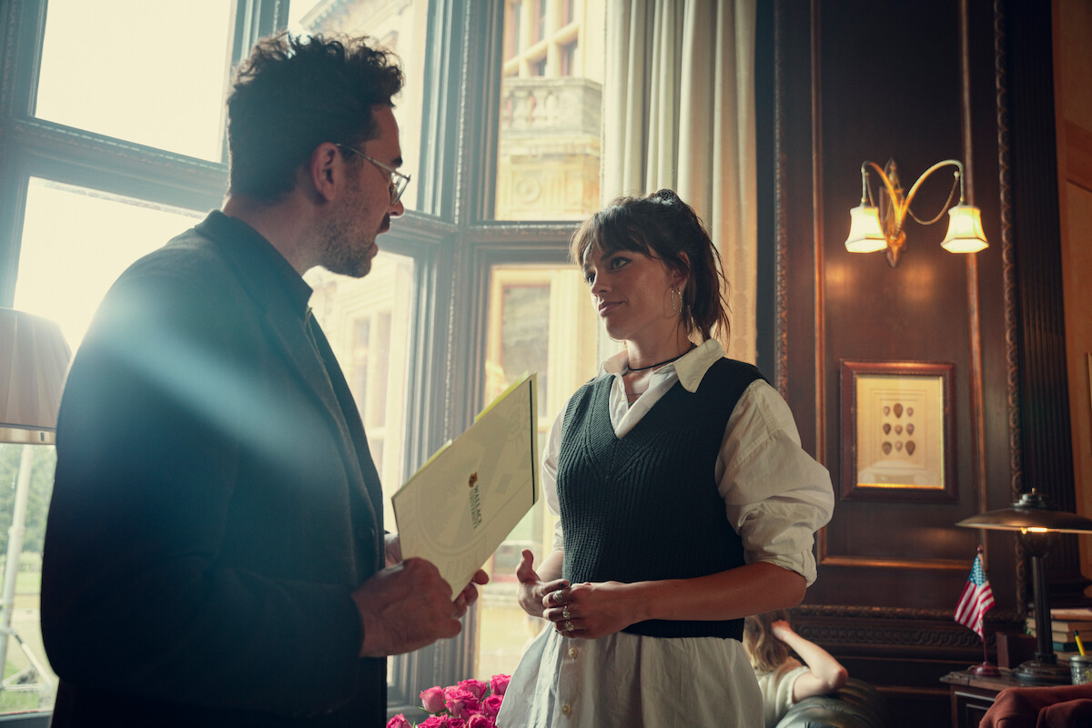  Dan Levy as Thomas and Emma Mackey as Maeve speak together in an office in Season 4 of ‘Sex Education.’ 