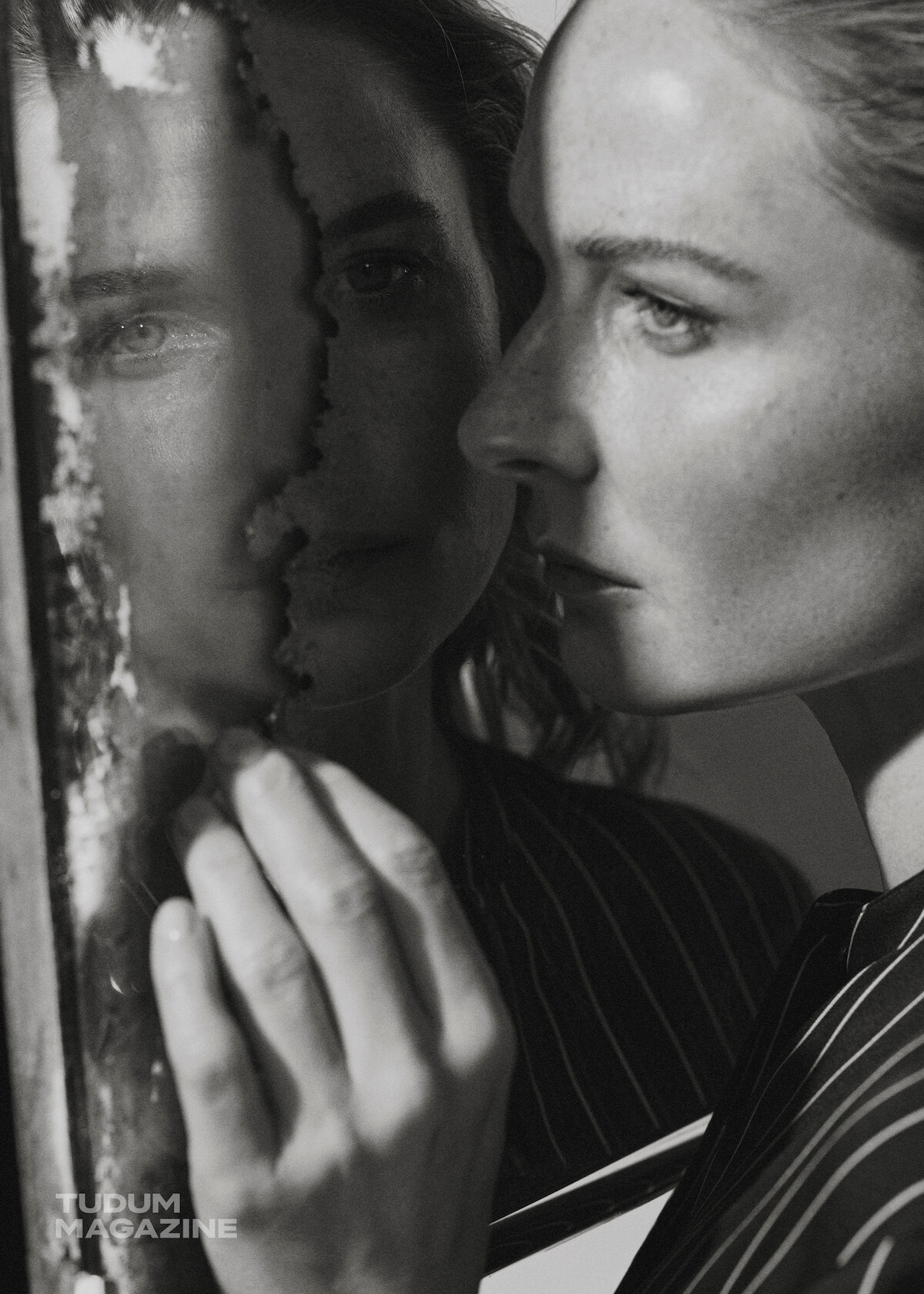 Rebecca Ferguson looks at herself in a mirror while wearing a pin stripe blazer.