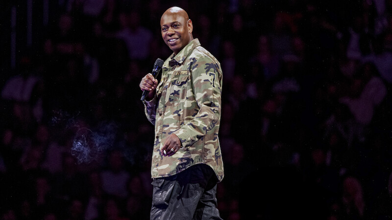 Dave Chappelle on stage holding a microphone.