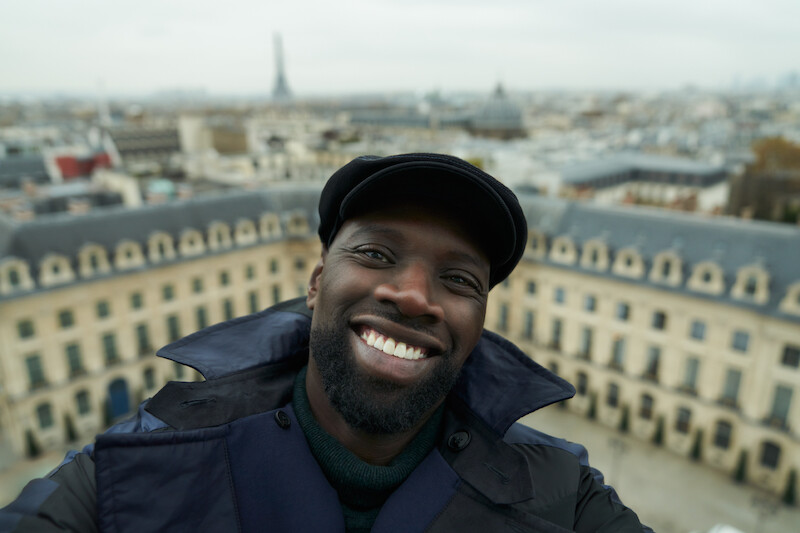 Omar Sy as Assane Diop smiles with the city of Paris in the background in Season 3 of 'Lupin.'