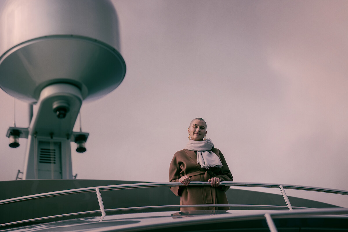 Lisa Loven Kongsli with a shaved head stands on deck aboard a yacht and looks down below with a smile.