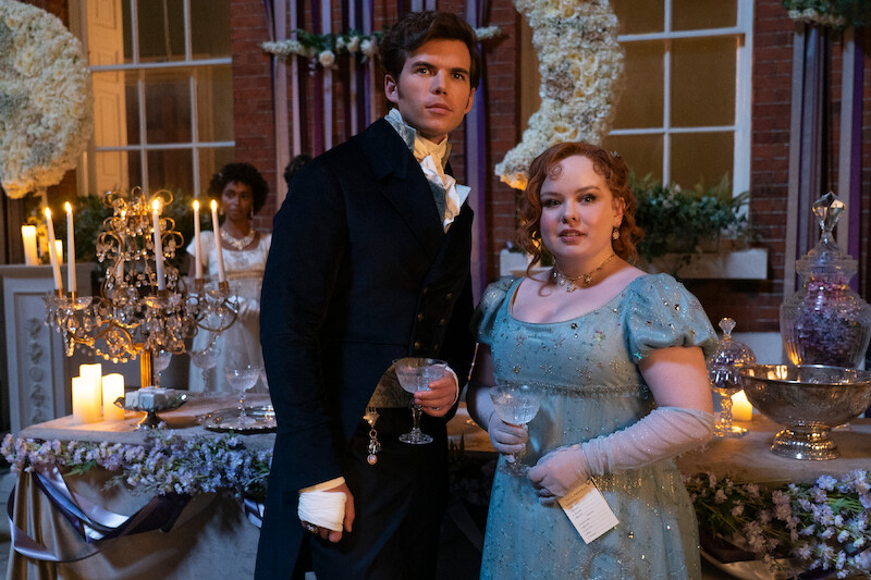 Bridgerton actors in costume standing in front of a table