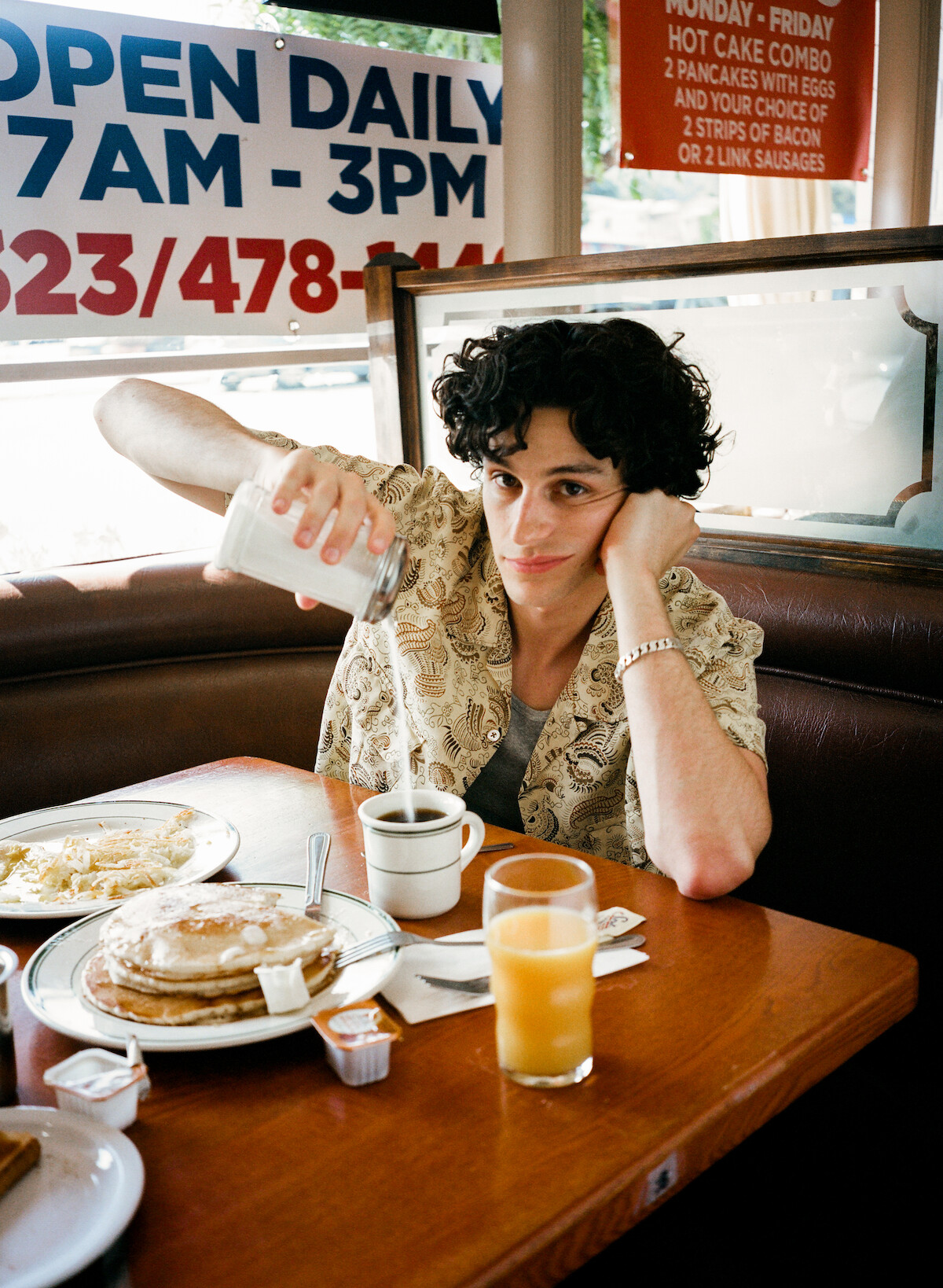 Owen Painter sitting at a diner table pouring sugar into his coffee and looking at the camera.