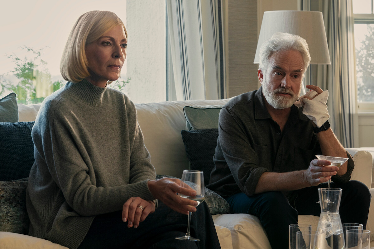 Allison Janney as Grace Penn with a wine glass in-hand sits down next to Bradley Whitford as Todd Penn who holds a cocktail glass in one hand while his other hand is wrapped in a cloth bandage.
