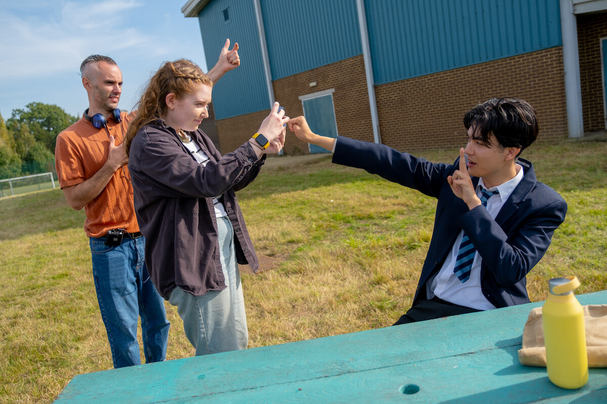 Behind the scenes image of Alice Oseman taking a photo of William Gao as Tao on the set of Season 3 of ‘Heartstopper’