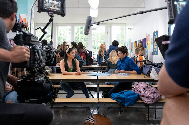 Lana Condor as Lara Jean and Noah Centineo as Peter Kavinsky talking at a lunch table.