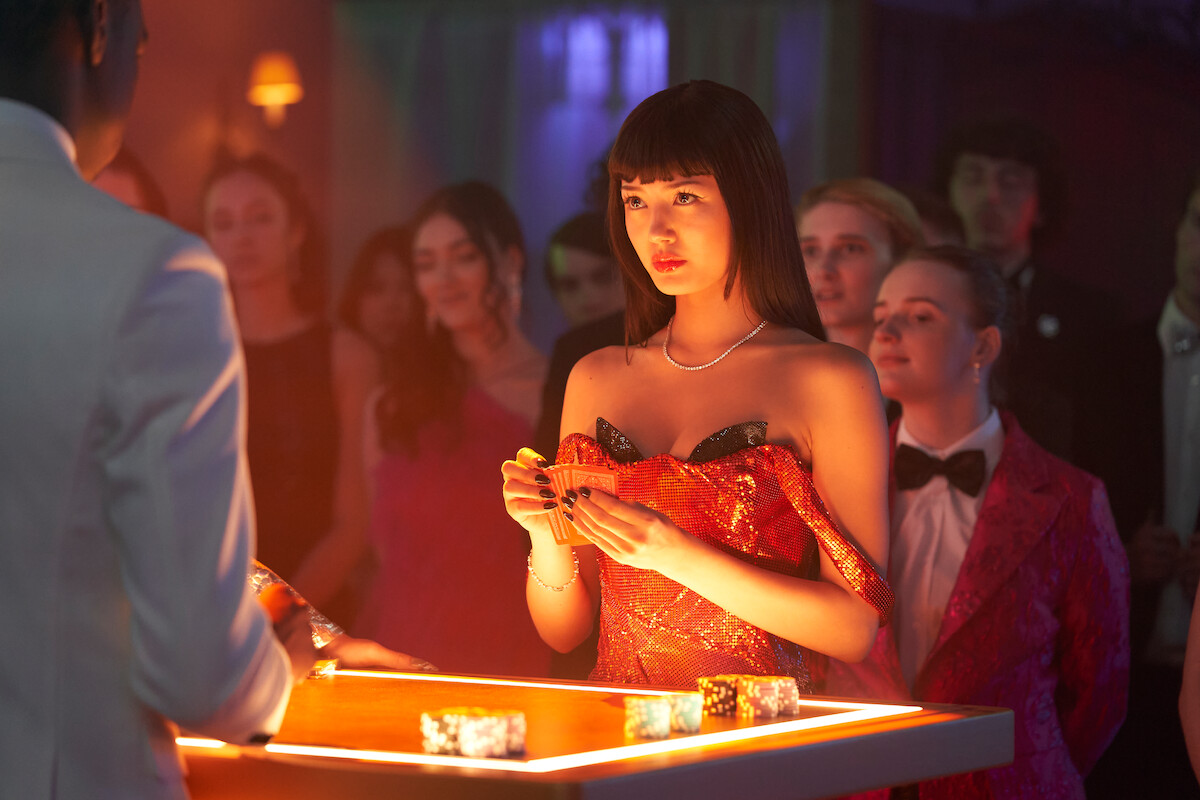 Miku Martineau stands at a table with poker chips on it as she holds a hand of cards in an image from the series ‘Bet.’