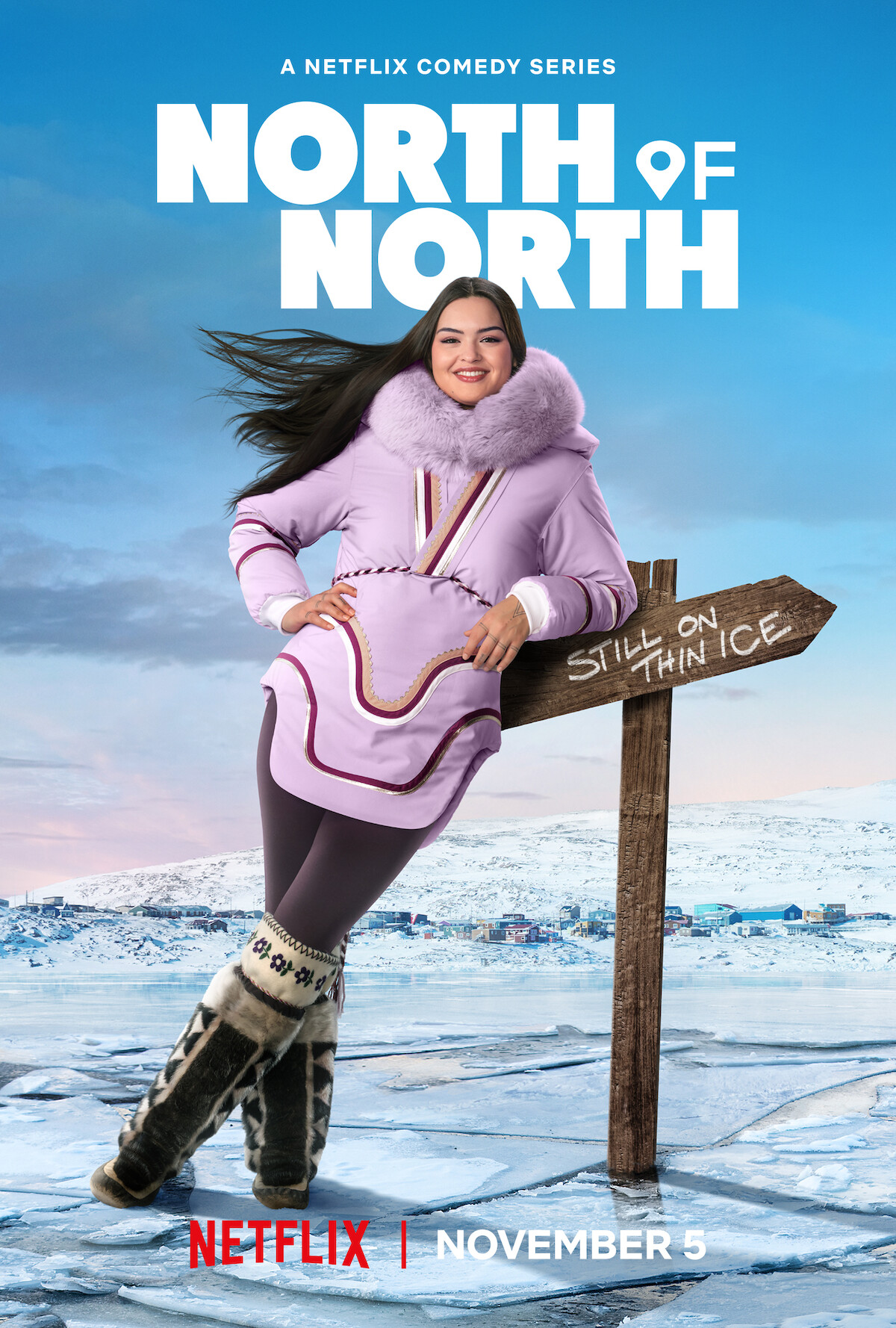 Smiling woman in a purple parka stands outdoors on ice with a wooden sign reading "Still on Thin Ice", snowy arctic town and mountains in background, blue sky; promotion for Netflix comedy series "North of North," premiering November 5.