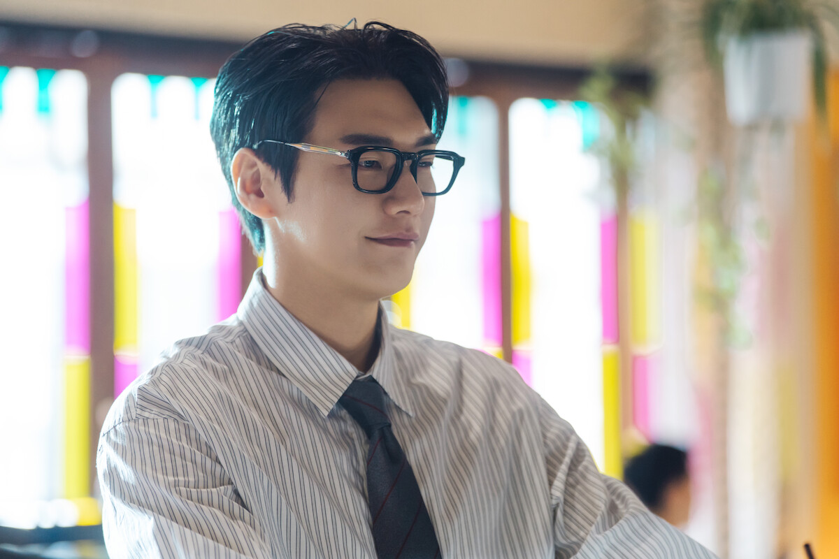 Um homem sul-coreano veste camisa listrada, gravata azul escura e óculos pretos