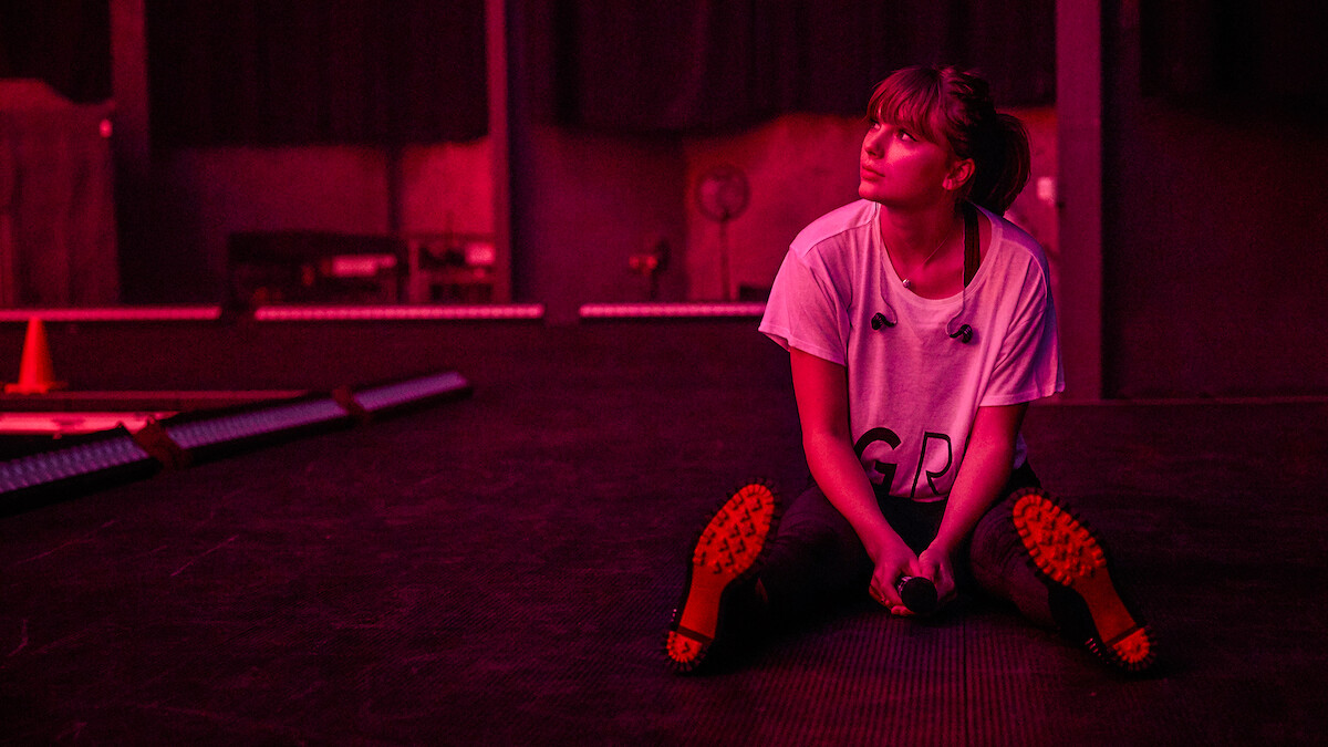 Artist Taylor Swift in recording studio bathed in magenta spotlight.
