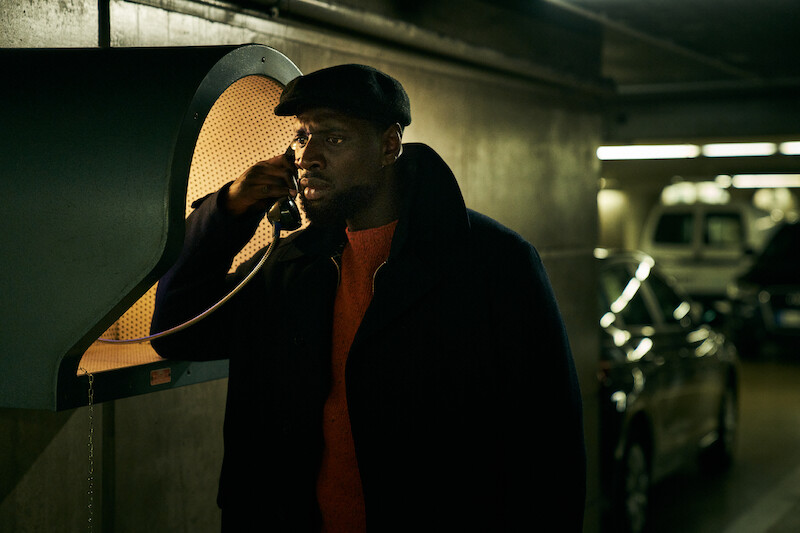 Omar Sy as Assane Diop makes a call at a payphone in Season 3 of 'Lupin.'