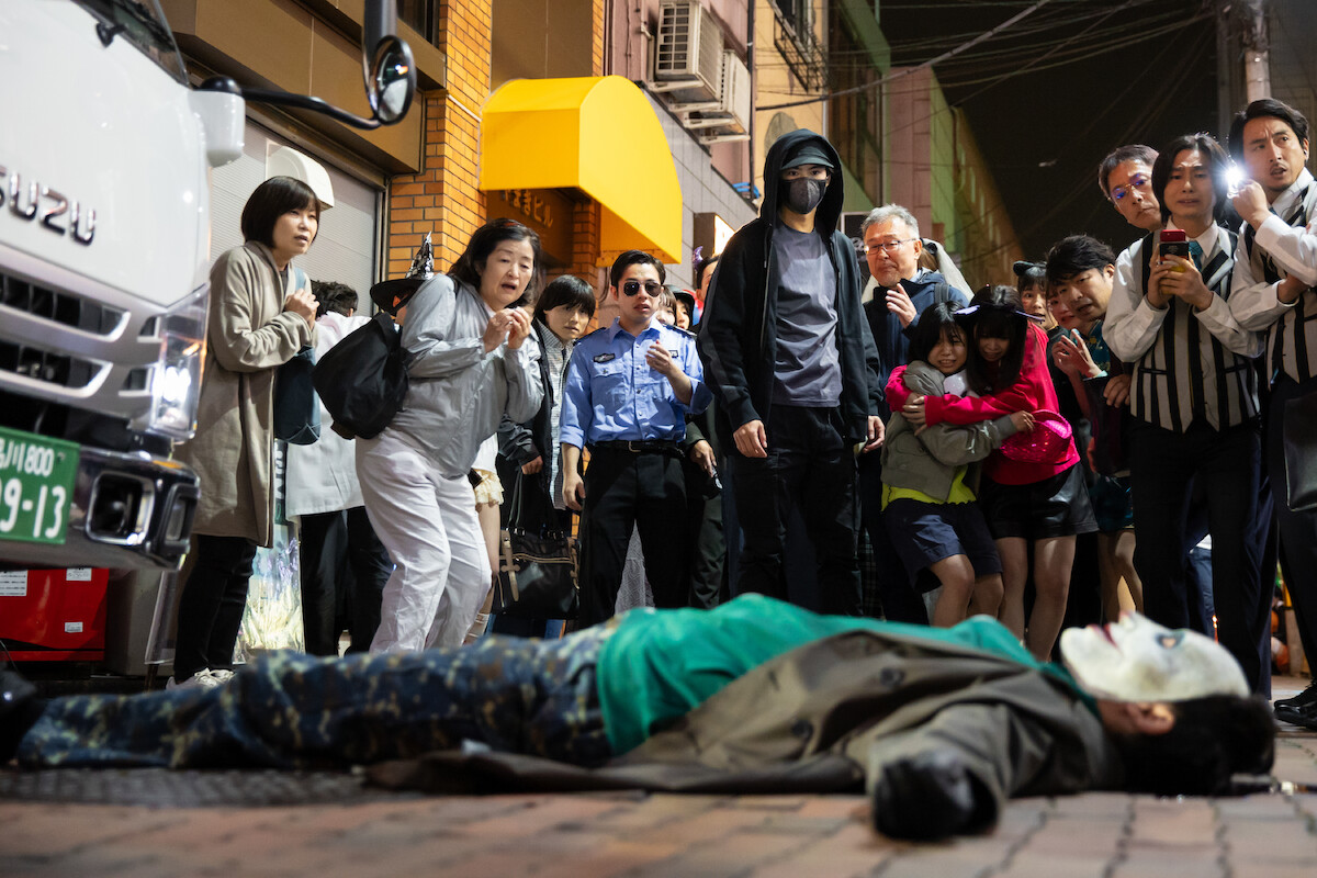 Kento Kaku as Haru Tawara stands in a crowd of people as they look on in horror at a body on the ground in a still image from the series ‘House of Ninjas’