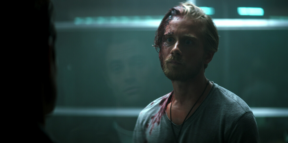 A bloody Benji (Lou Taylor Pucci) looks out through the cage