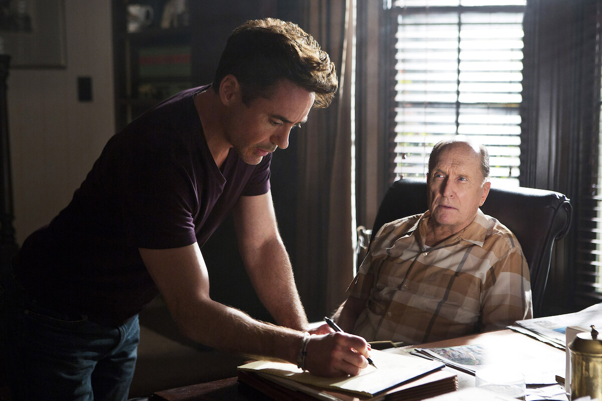 In an image from the film ‘The Judge,’ Robert Downey Jr. leans over a desk to write something down as Robert Duvall looks at him from his seat.