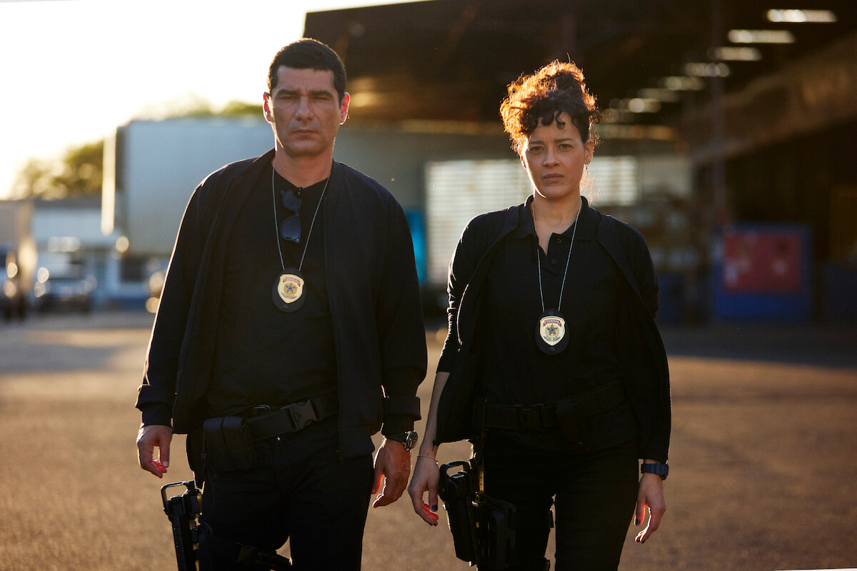 Rômulo Braga as Benício and Maeve Jinkings as Suellen stand together in police uniform in the series ‘Criminal Code’