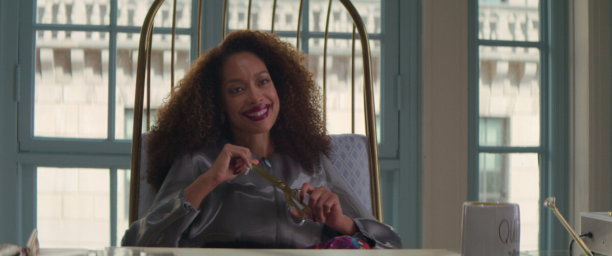 Gina Torres sits behind a desk in a iridescent purple blazer in a still from ‘The Perfect Find.’