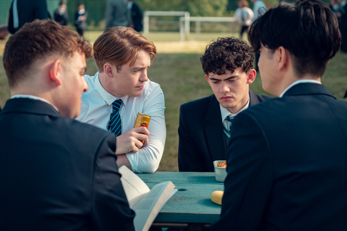 Kit Connor as Nick and Joe Locke as Charlie sit at a picnic bench at school with concerned expressions in Season 3 of ‘Heartstopper.’