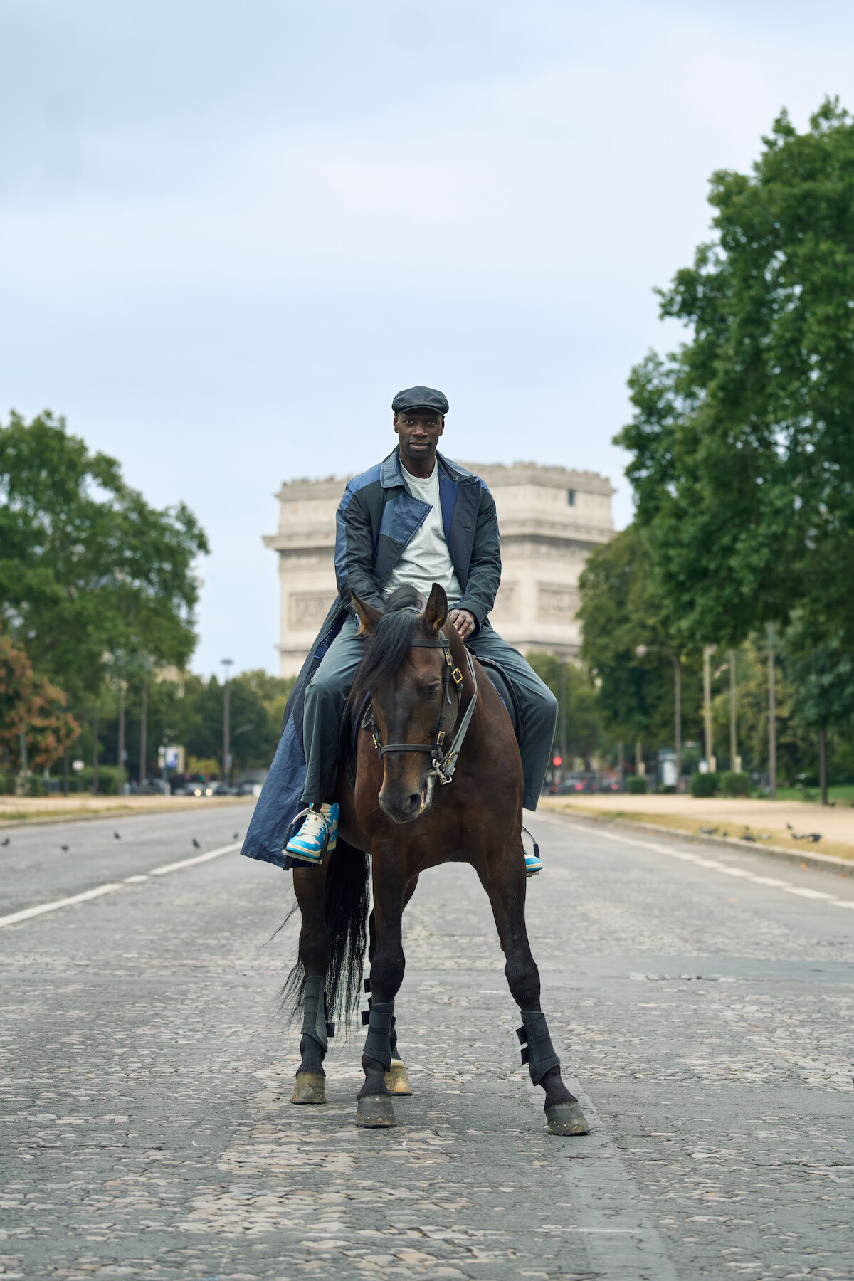 Um homem negro, de sobretudo e chapéu azul marinho, aparece montado em um cavalo marrom em uma rua de Paris