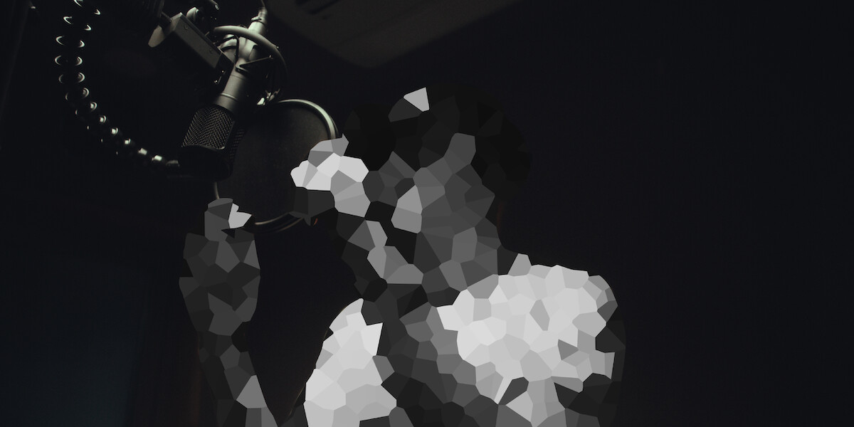 Person recording vocals in a dimly lit studio, standing in front of a microphone, image is pixelated for privacy.