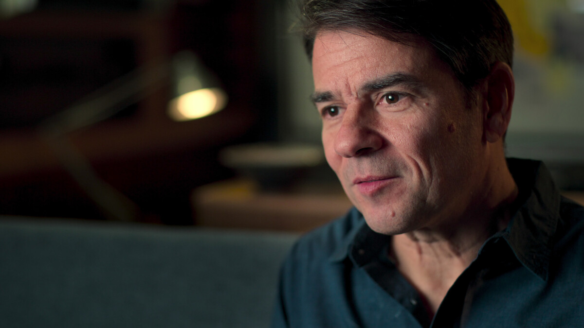 A white man in a collared shirt looks contemplatively at the interviewer.