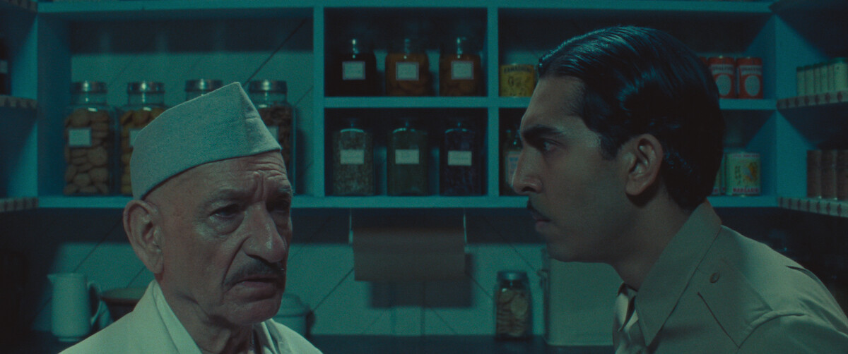Ben Kingsley as Dr. Ganderbai and Dev Patel as Woods converse in a pantry in ‘Poison.’