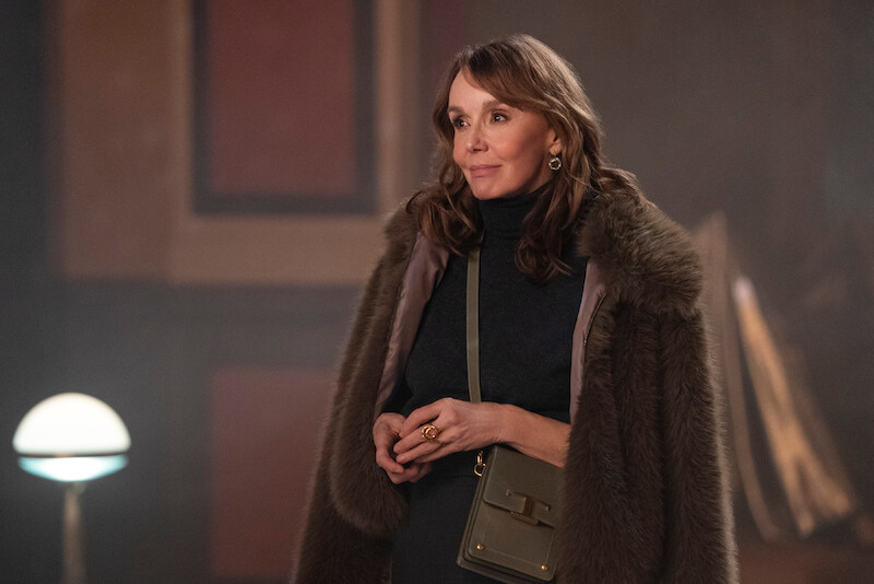 Philippine Leroy-Beaulieu as Sylvie Grateau smiles and wears a coat over her shoulders in Season 4 of 'Emily in Paris'