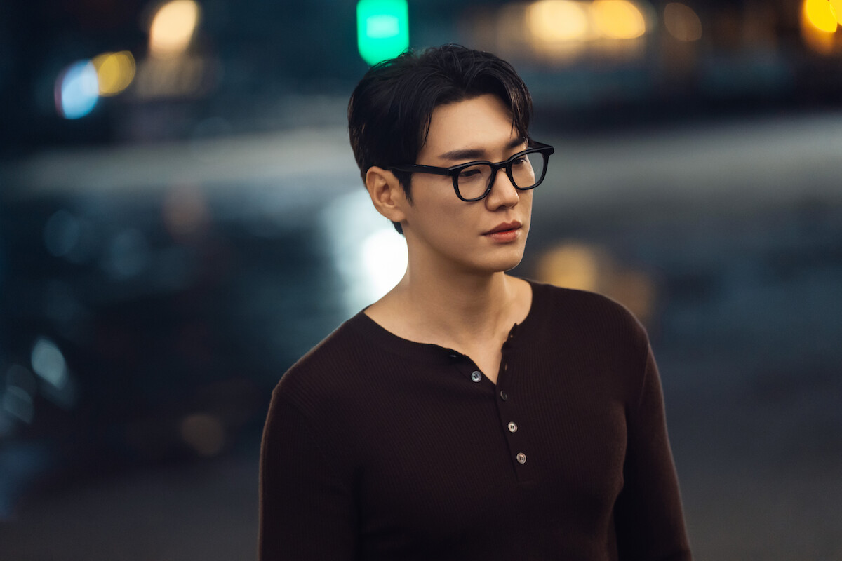 Um homem sul-coreano jovem usa óculos e camisa marrom
