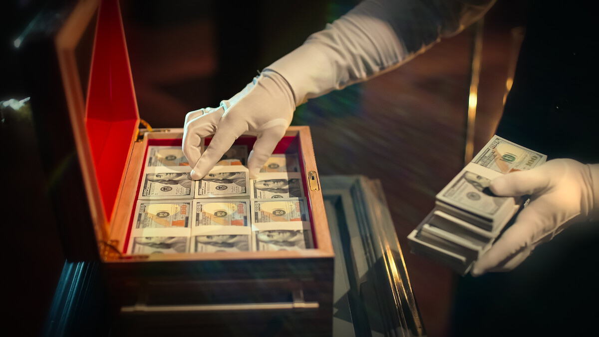 A wooden box filled with cash is handled by someone in white gloves in 'Million Dollar Secret.'