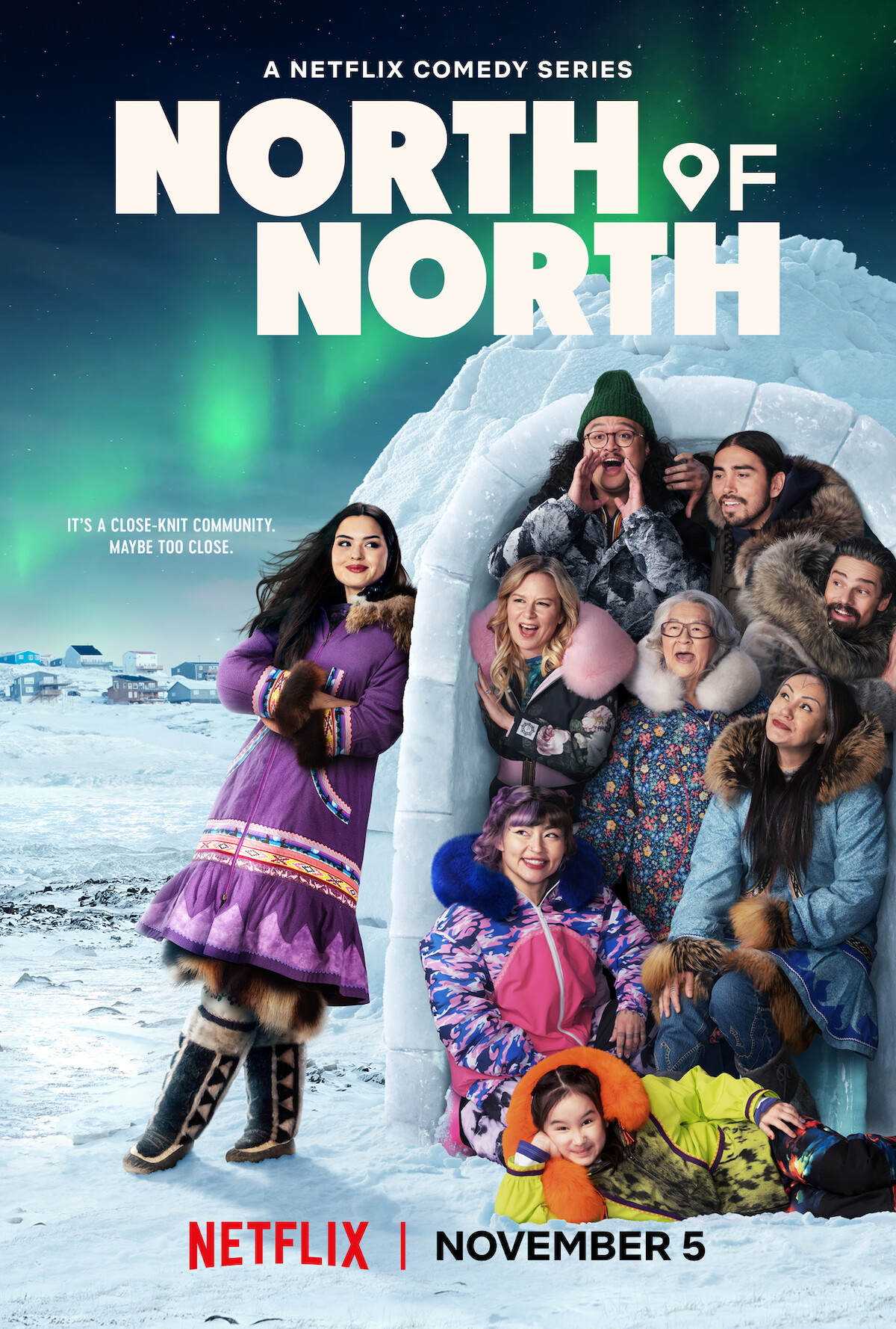 Group of people in colorful winter clothing pose cheerfully around and inside an igloo in a snowy Arctic village, with the northern lights glowing in the night sky above them; Netflix comedy series promo.