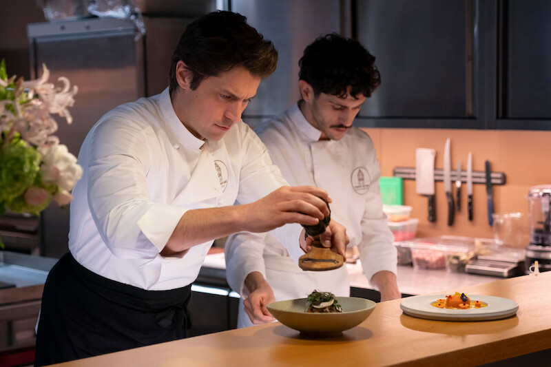  Lucas Bravo as Gabriel plates food in a kitchen in Season 4 of 'Emily in Paris'