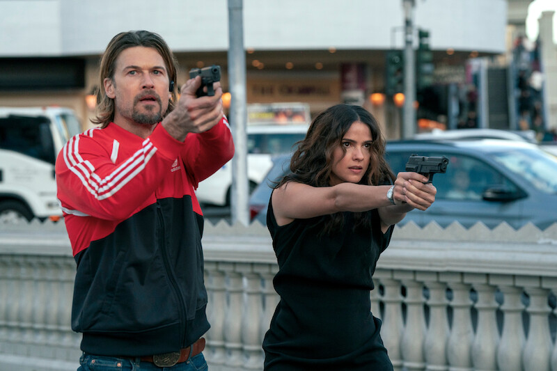 Nick Zano as Chad McKnight and Shelley Hennig as Ava Winters hold up their guns together in Season 1 of 'Obliterated.'