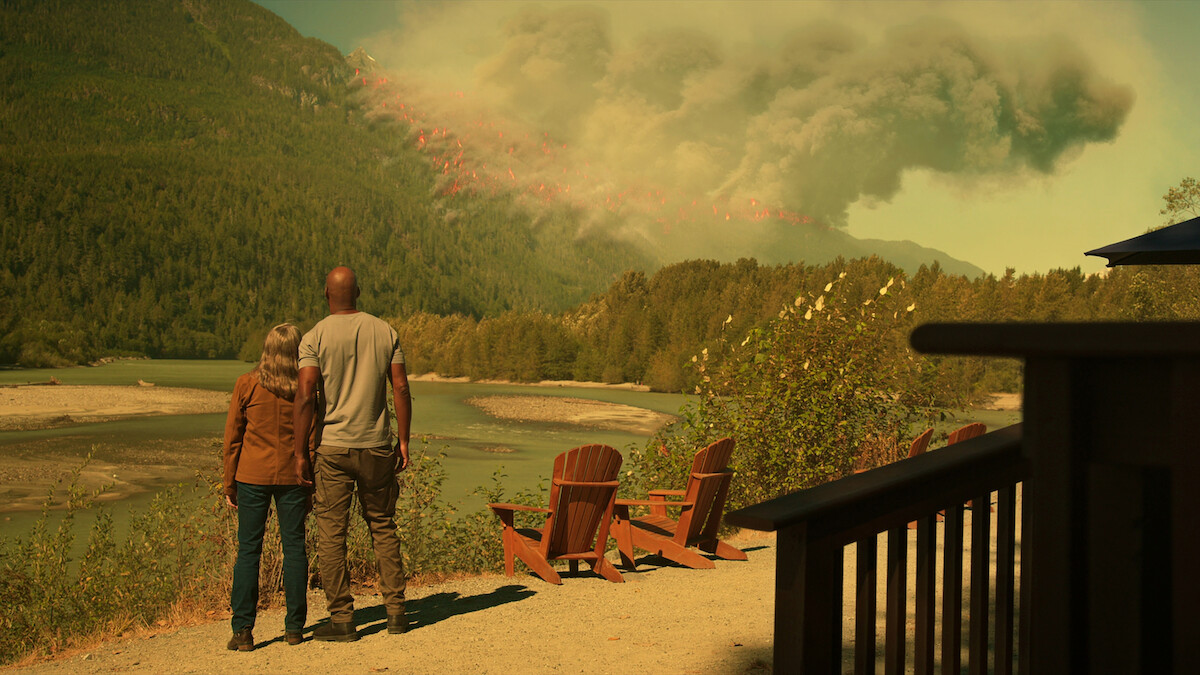Annette O’Toole as Hope and Colin Lawrence as Preacher stand together and watch a wildfire blaze through the mountainside in Season 5 of ‘Virgin River.’