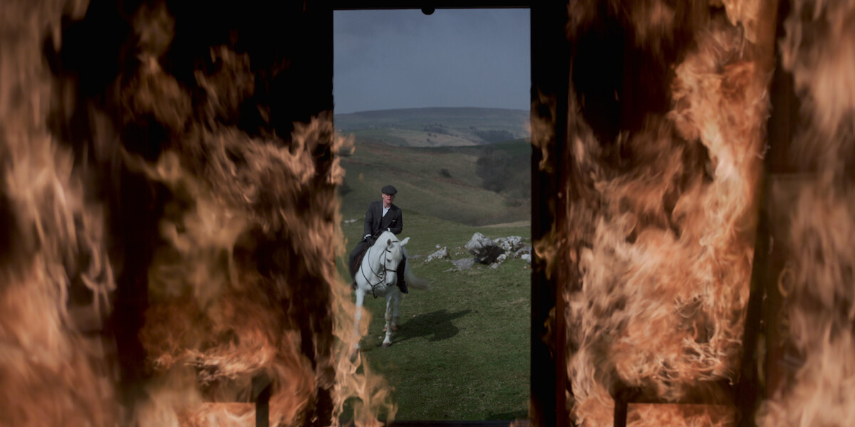 A man on a white horse looks at a burning building.