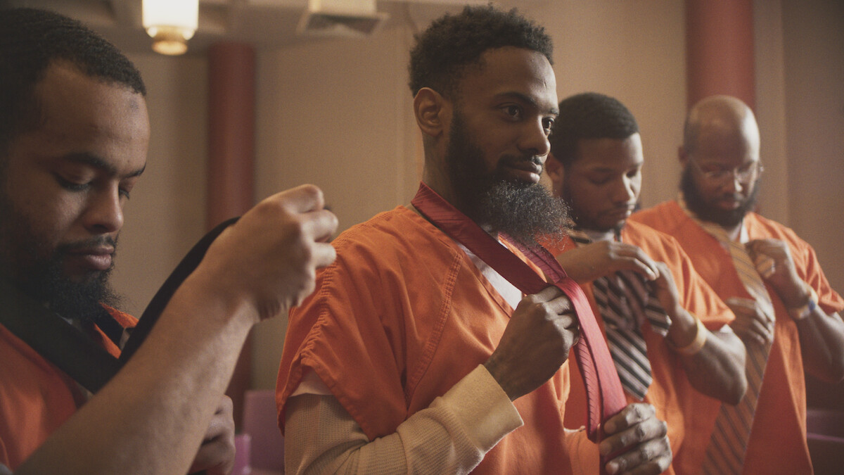 Donte Brooks, Allan James, Leonard Smith, and Jeffrey Saunders tie their ties over orange jumpsuits.
