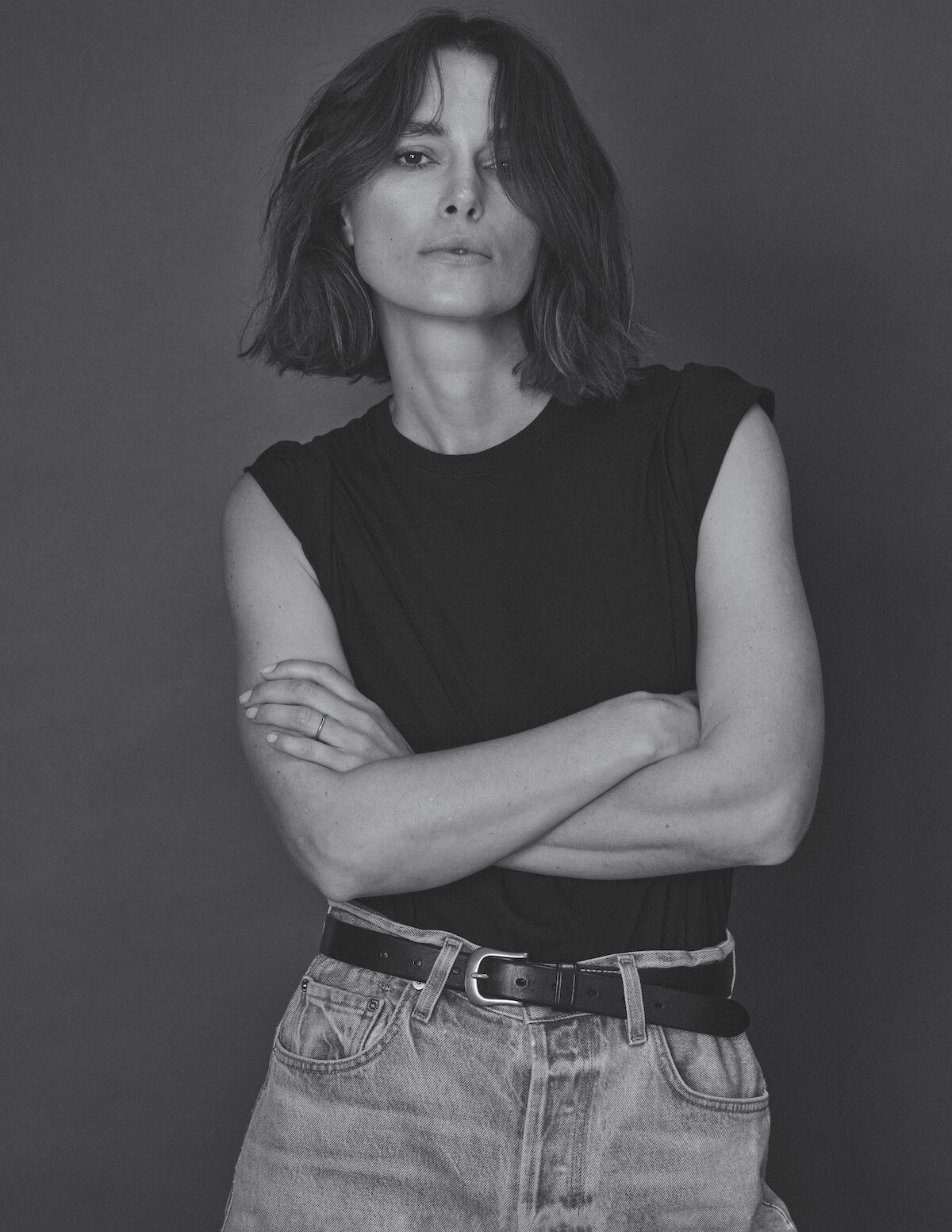 Keira Knightley wears a black muscle tank and jeans and crosses her arms in a Rosie the Riveter-esque Stance.