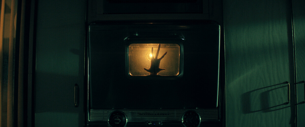 A silhouette of a hand with splayed fingers presses against an oven window in ‘The Boroughs’