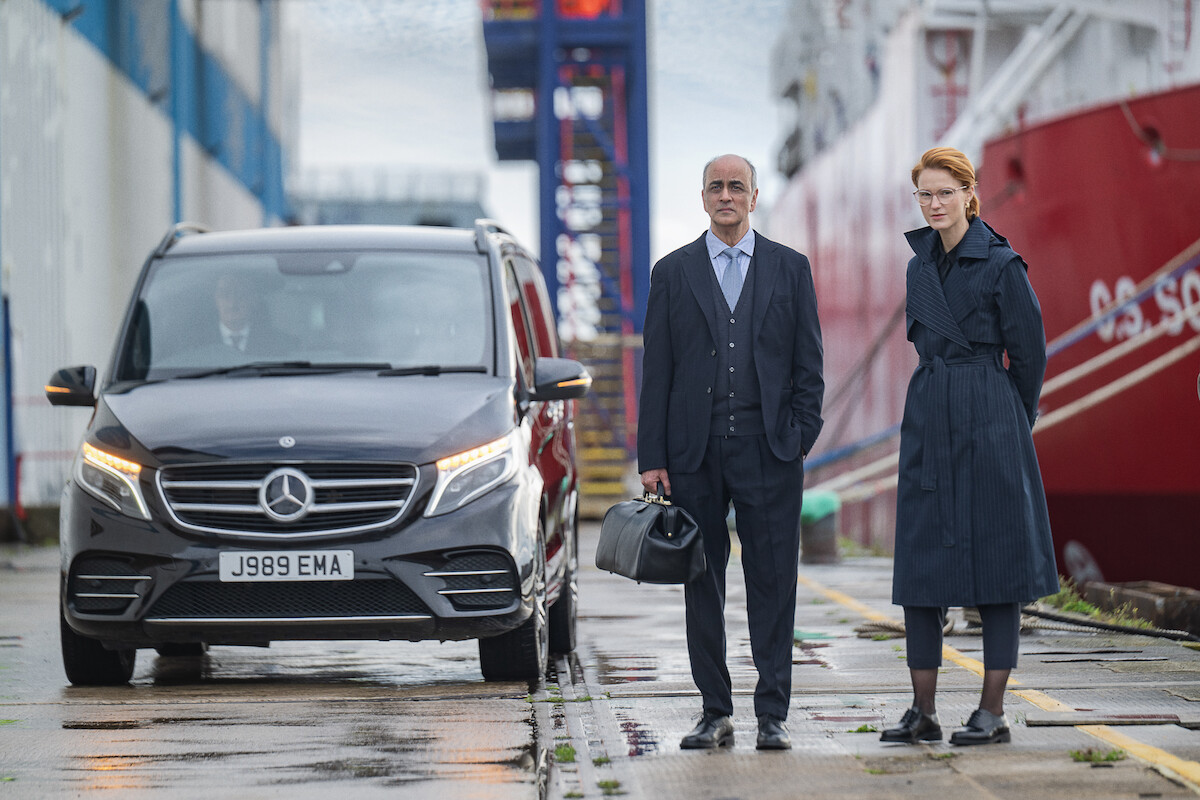 A man and a woman in formal clothes stand near a black van.
