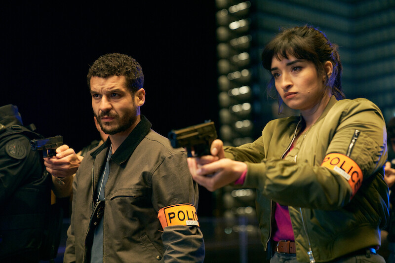 Soufiane Guerrab as Youssef Guedira and Shirine Boutella as Lieutenant Sofia Belkacem stand together holding guns in Season 3 of 'Lupin.'