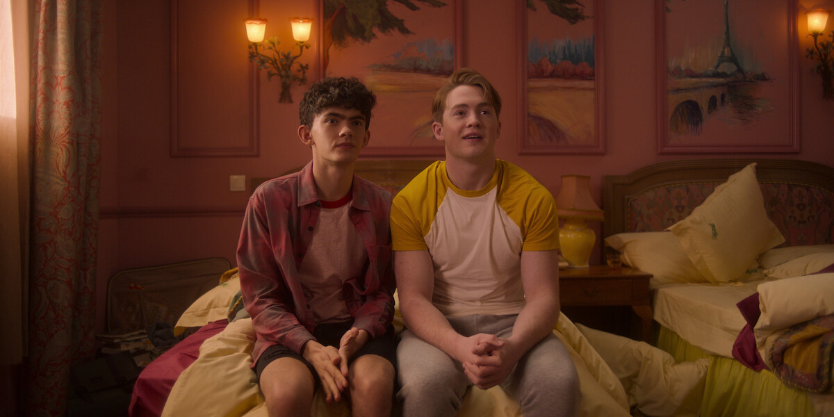 Joe Locke as Charlie and Kit Connor as Nick sit together on a bed in a hotel room in Season 2 of ‘Heartstopper.’