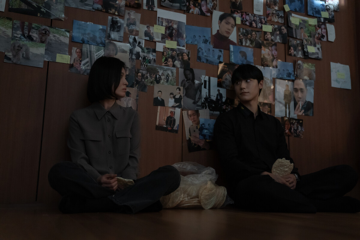 Two people sitting down against a wall plastered with photographs.