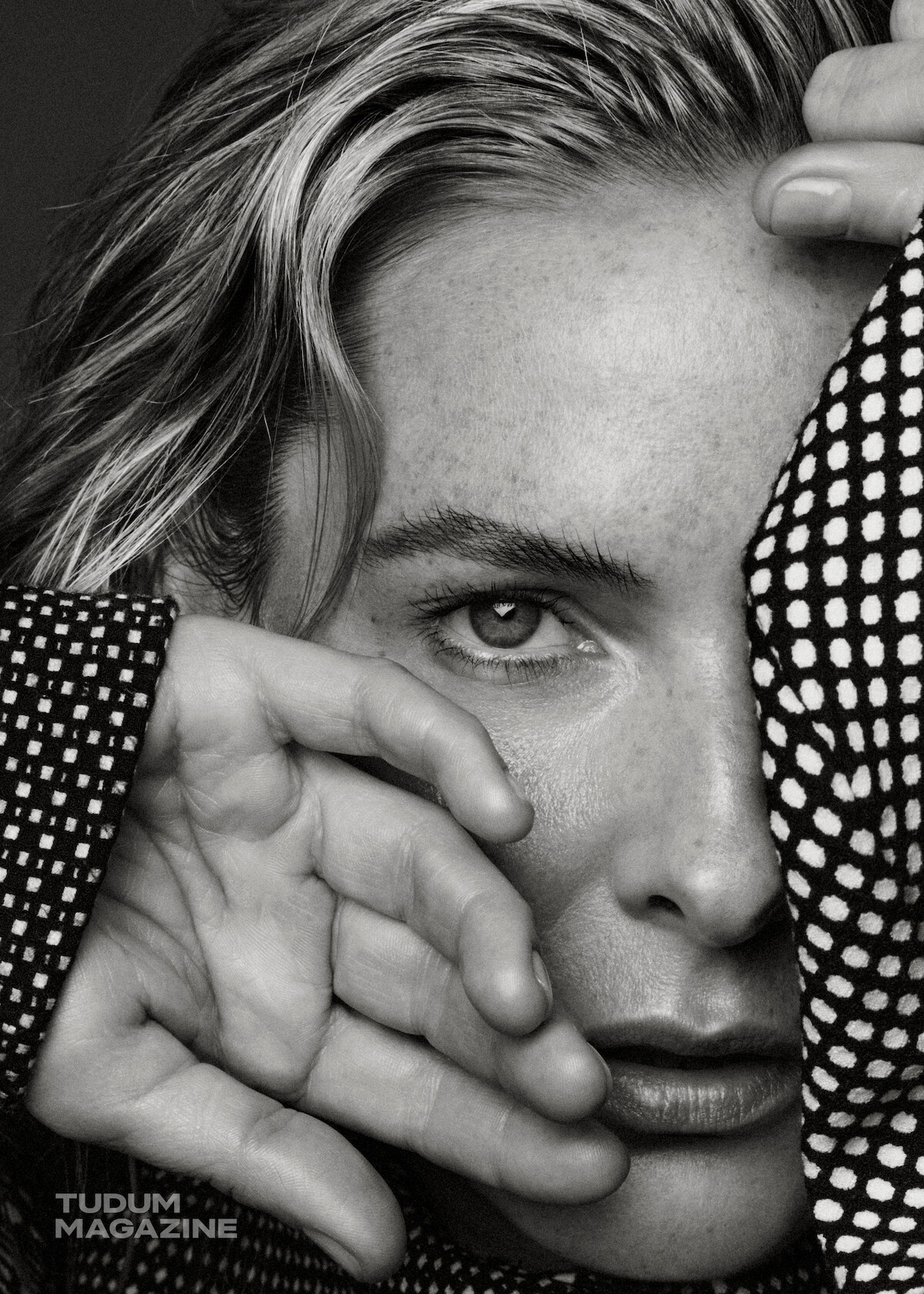 Rebecca Ferguson, wearing a polka-dot blouse, covers her face with her hands.