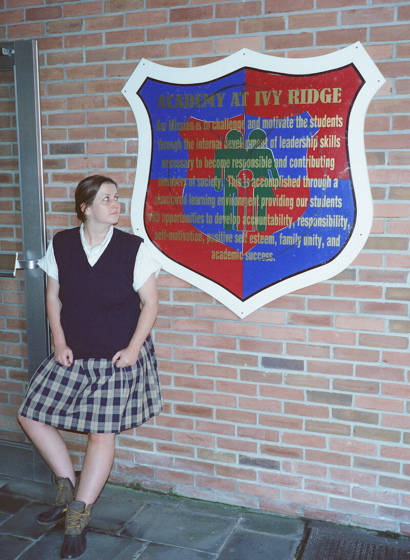 Student standing in front of The Academy at Ivy Ridge crest. 